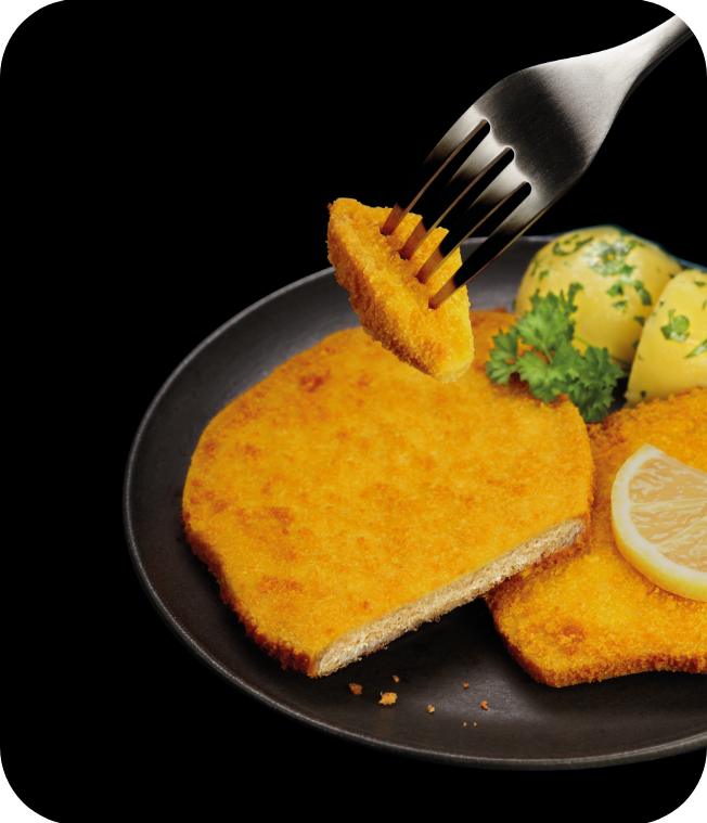 Knuspriges Schnitzel mit Zitronenscheibe, Petersilienkartoffeln und einer Gabel mit einem Stück Schnitzel.